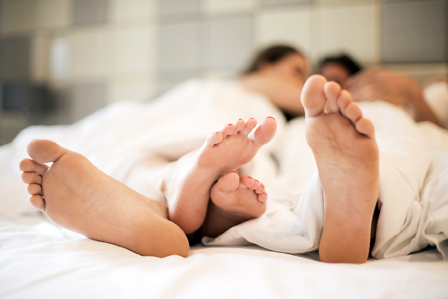 Image d'en-tête de l'article Je Réalise " Comment aborder la sexualité en 10 points ? ", sur laquelle l'on voit un couple allongé sur un lit dans des draps, leurs pieds entremêlés au premier plan.