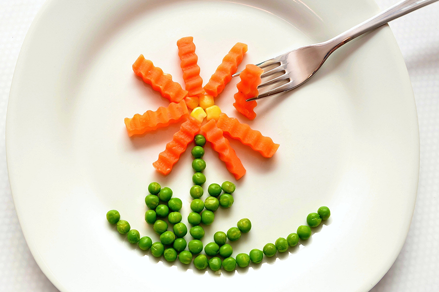 Image d'en-tête de l'article Je Réalise " Booster mon énergie #1 Par l'alimentation ", sur laquelle l'on voit une assiette blanche et une fourchette en train de prendre un morceau d'une fleur composée de maïs, de carottes et de petits pois.