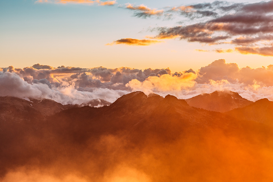 Image d'en-tête de l'article Je Réalise " Vivre en paix ", sur laquelle nous sommes au-dessus des montagnes et des nuages. Une lueur jaune orangé laisse deviner la présence prochaine du soleil.
