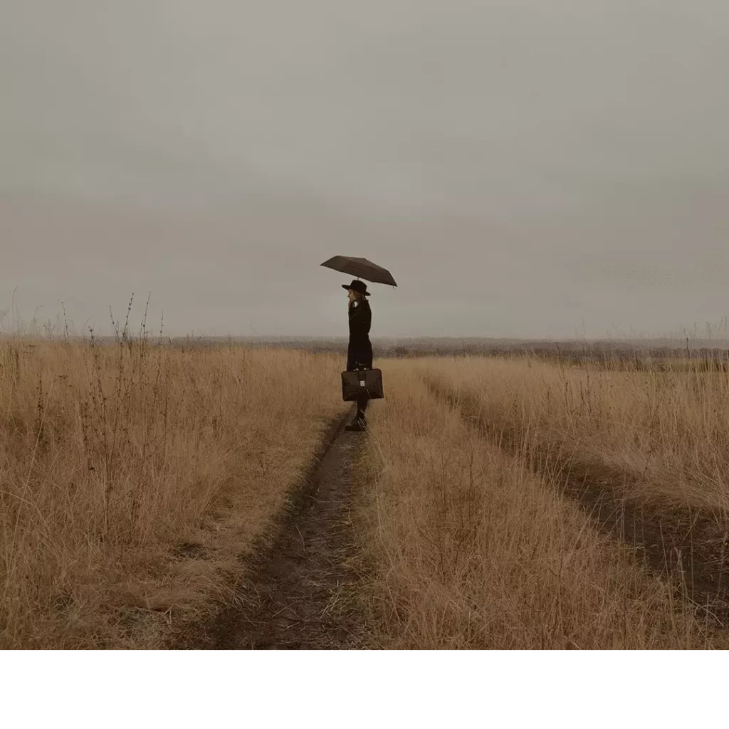 Image d'en-tête de l'article Je Réalise : " Apaiser la tristesse ", sur laquelle l'on voit une personne tournée vers la gauche, seule dans un champ, tenant un parapluie sous un ciel gris.