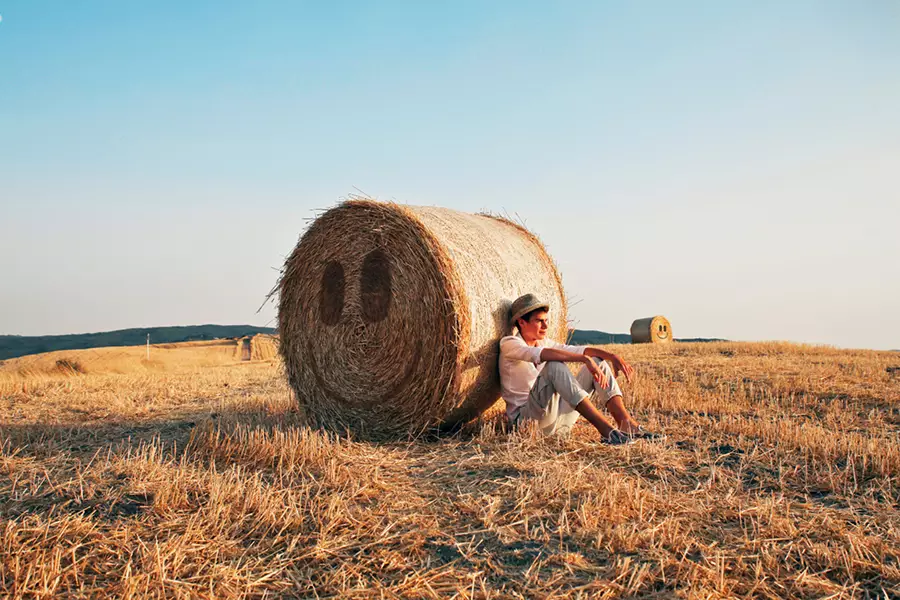 Image d'en-tête de l'article Je Réalise " 5 astuces pour prendre la vie du bon côté #2 ", sur laquelle l'on voit un adolescent adossé à un ballot de paille portant un Smiley souriant, dans un champ au soleil couchant.