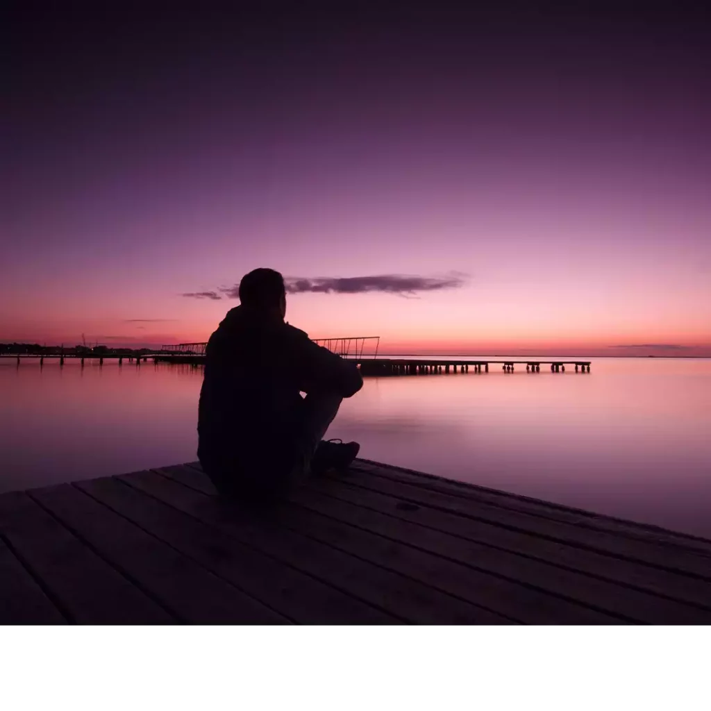 Image d'en-tête de l'article Je Réalise : " Apprivoiser nos émotions " ", sur laquelle l'on voit une silhouette d'homme assit sur un ponton au bord de l'eau contemplant les belles couleurs du crépuscule.